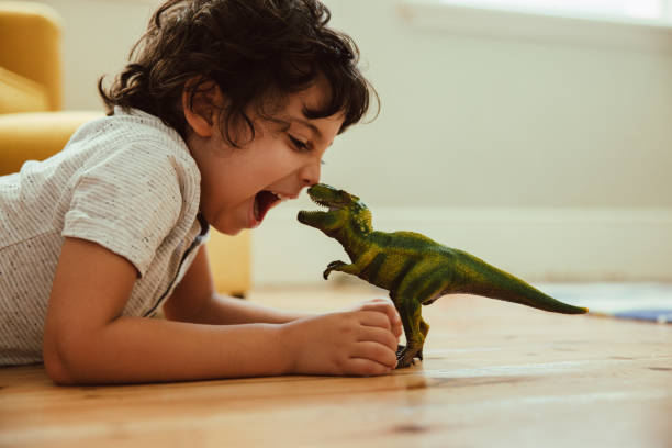 Adventurous young boy imitating a t-rex dinosaur toy at home