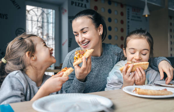 Happy mom and her two daughters eat pizza.