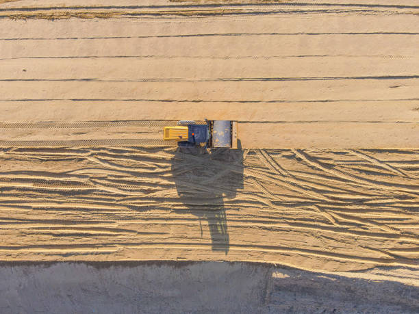 Construction roller view from above Construction roller view from above - photo of construction equipment on a sand road. Construction roller on the sand. A grader on the sand. Bulldozer on the sand. A sandy road. Shadow of construction equipment on the sand. Road grader leveling sand. Roadbed worker. Photo from a drone. road scraper stock pictures, royalty-free photos & images