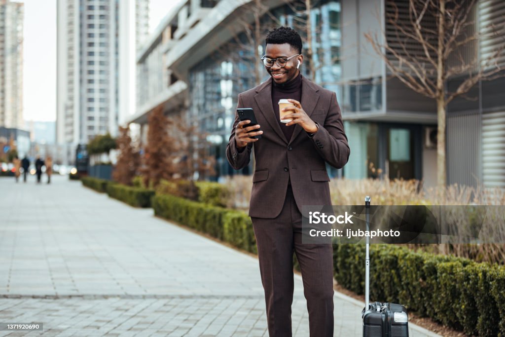 Smiling businessman with smart phone and cup Shot of a businessman walking around town with his luggage while using his smartphone and coffee to go. Businessman Stock Photo