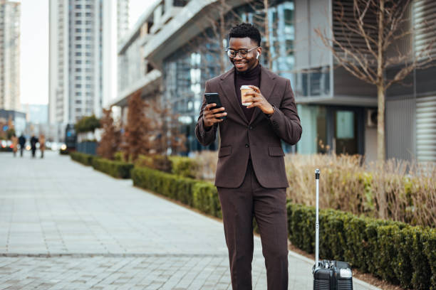 улыбающийся бизнесмен со смартфоном и чашкой - walking people business travel business стоковые фото и изображения