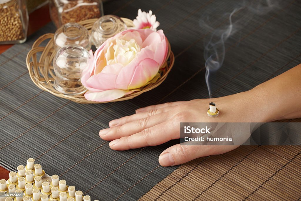 Mini moxa stick therapy TCM Traditional Chinese Medicine. Smoking mini moxa stick, flower and natural herbs in glass jars in background. Moxa Stock Photo