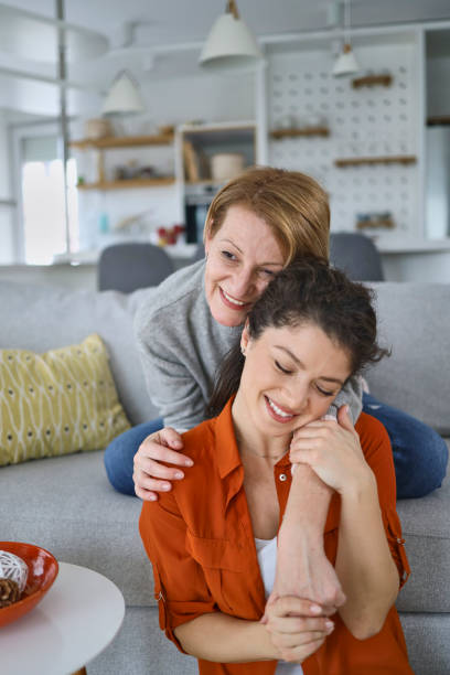 Portrait of a senior mother and adult daughter, hugging, smiling in the living room stock photo