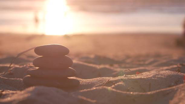 Stack of pebble stones, sandy ocean beach, sunset sky. Rock balancing by water.