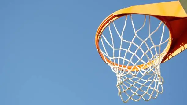Photo of Basketball court outdoors, orange hoop, net and backboard for basket ball game.
