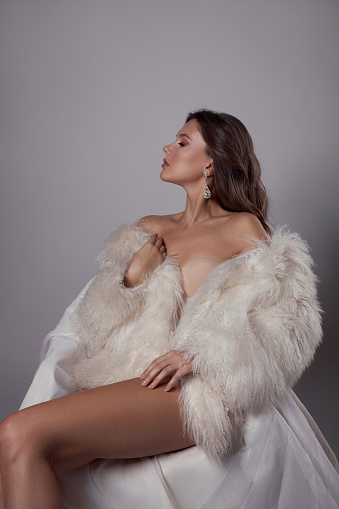 Beauty art portrait of a beautiful woman with long hair, white fur coat with long faux fur. Beautiful earrings in a woman's ears. Hairstyle, hair styling