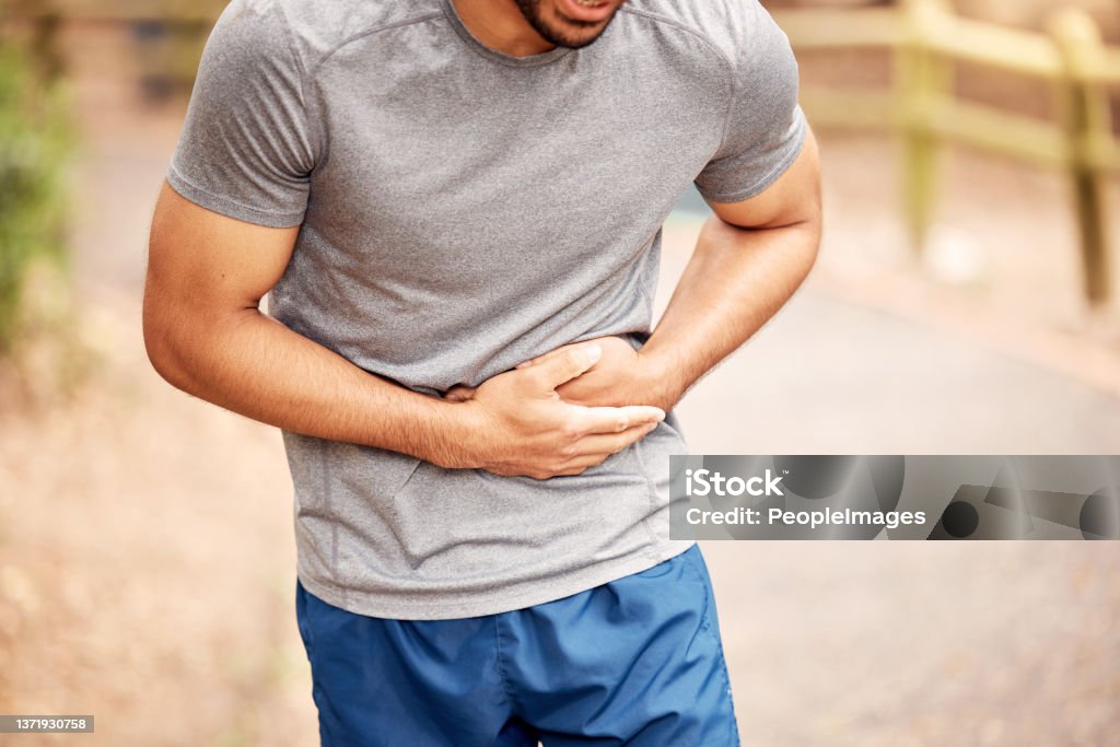 Shot of an unrecognisable man experiencing stomach ache while working out in nature Pain doesn't have to be the end of your fitness journey Hernia Stock Photo