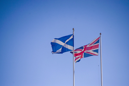The national flag of Scotland and the Union Jack flag with a clear blue sky background.