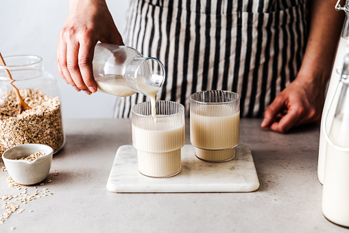 Close-up of a woman pouring oat milk in glasses