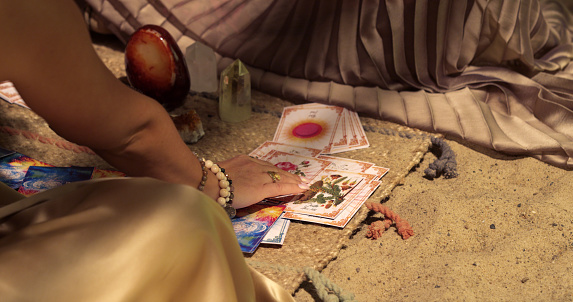 Beautiful female artist sitting on the floor, using palo santo smoke and divination cards. Tent in desert oasis