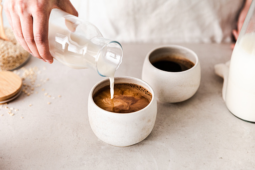 Close-up of pouring oat milk into a black coffee c