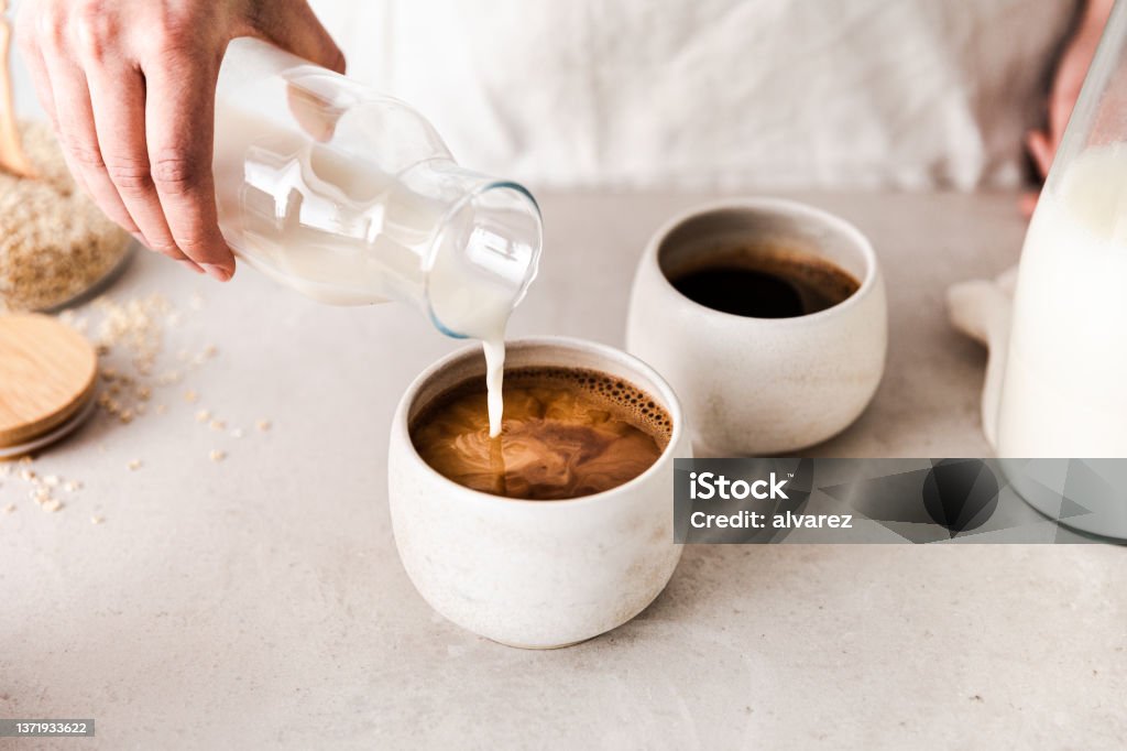 Close-up of pouring oat milk into a black coffee c Close-up of pouring oat milk into black coffee cup. Making coffee at home. Coffee - Drink Stock Photo