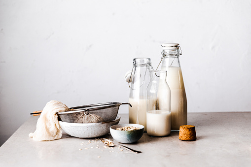 Vegan oat milk bottles with kitchen utensils on table. Preparing non dairy alternative milk with oat flakes.