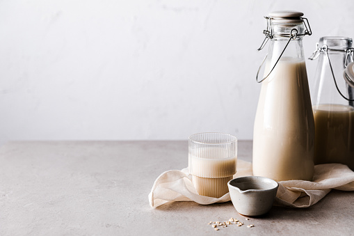 Glass of vegan milk with ceramic bowl and oat milk bottles. Homemade oat milk on kitchen table.