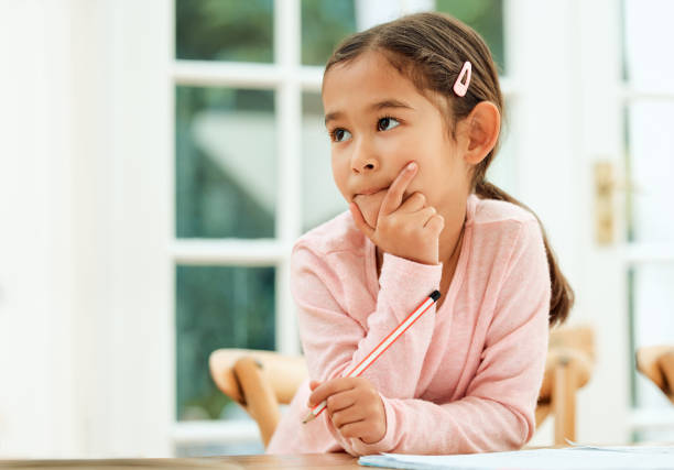 zugeschnittene aufnahme eines entzückenden kleinen mädchens, das nachdenklich aussieht, während es seine hausaufgaben macht - child thinking writing little girls stock-fotos und bilder