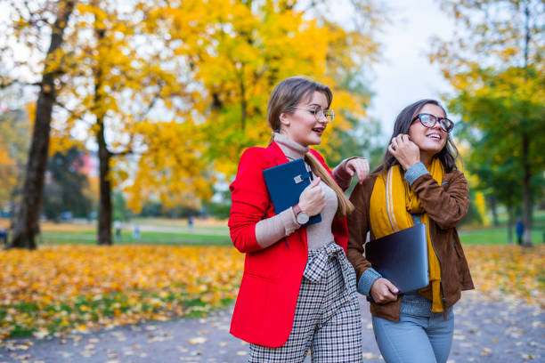 Two young female coworker walking in autumn park stock photo