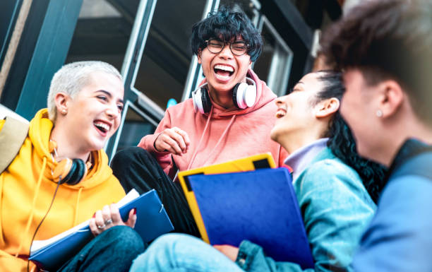 Multiracial students having fun together sitting outside school - Happy best friends enjoying time in college campus - Youth lifestyle and scholarship concept stock photo