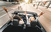 Happy couple driving on city street in convertible car - Friends rent cabrio auto on vacation - Roadtrip, freedom, travel and transport rental service concept