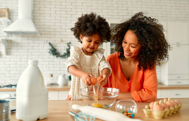 African american family at home African American woman with her little daughter with curly fluffy hair having fun and making pastries in the kitchen. Mom and daughter cooking together. domestic kitchen photos stock pictures, royalty-free photos & images