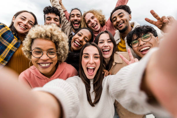 multiracial friends taking big group selfie shot smiling at camera - laughing young people standing outdoor and having fun - cheerful students portrait outside school - human resources concept - jong volwassen fotos stockfoto's en -beelden