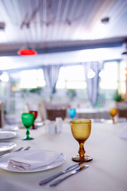 a yellow transparent glass close-up stands on the table against the background of a white tablecloth and other table setting items in blur