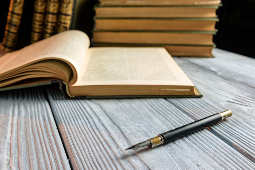 Antique fountain pen on the table with books. Literary composition with selective focus.