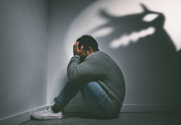 foto de un joven sentado en la esquina de una habitación oscura con una figura aterradora en la pared - atrapado fotografías e imágenes de stock