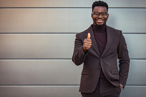 Shot of a young businessman showing a thumbs up in the city looking at camera.