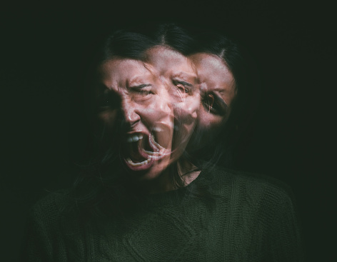 Studio shot of a young woman experiencing mental anguish and screaming against a black background