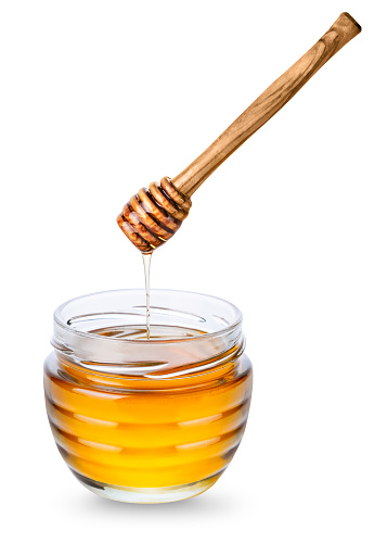 Glass jar with honey and wooden honey dipper with honey drop isolated on white background.