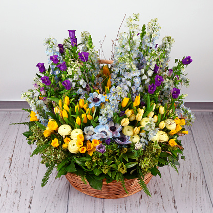 Flower arrangement with delphinium, campanula and tulips on light wooden floor