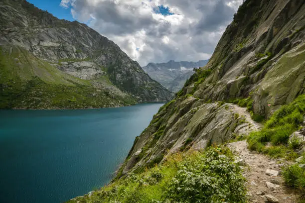 Dangerously looking walking trail next to stone wall above Gelmersee lake in Swiss Alps