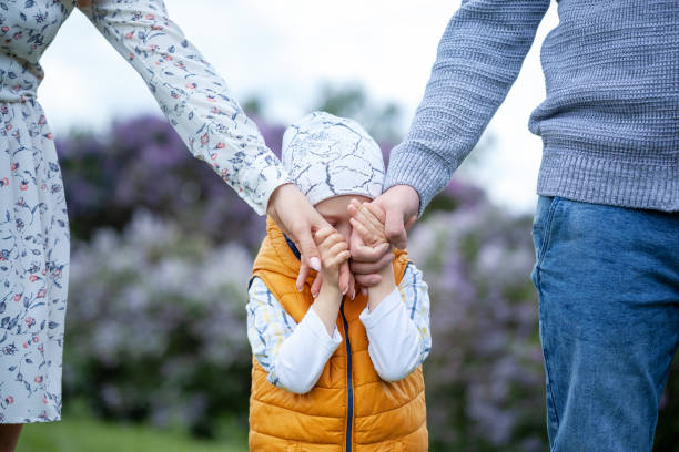 Son holding mother and father for hands. Child covers his face with his hands. stock photo