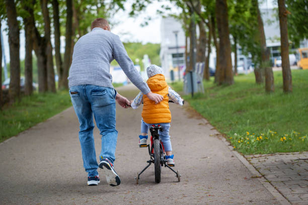 istock Father help son to ride bicycle in summer park. Back view 1371955084