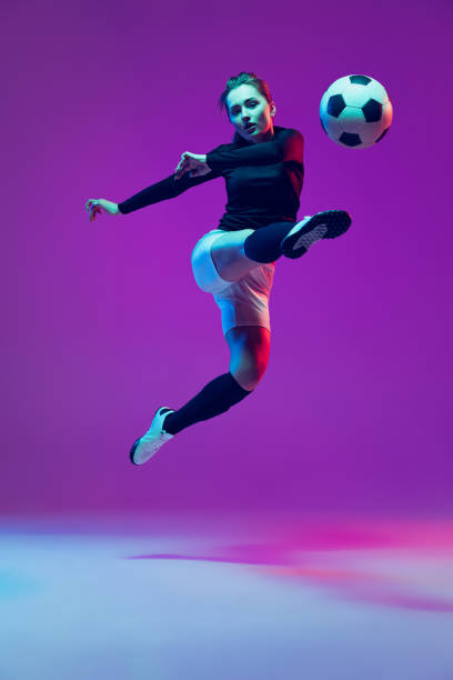 dynamisches porträt einer fußballspielerin, die mit einem fußball trainiert, isoliert auf lila studiohintergrund im neonlicht. sport, action, bewegung, fitness - exercising women sport studio shot stock-fotos und bilder