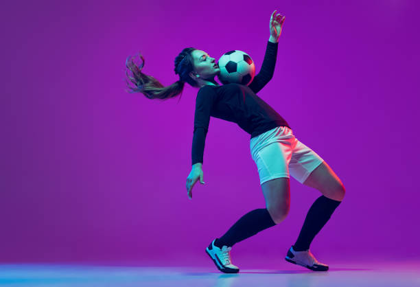 emotive girl, female soccer, football player in motion, action isolated on purple studio background in neon light. sport, active, healthy lifestyle - short cut imagens e fotografias de stock