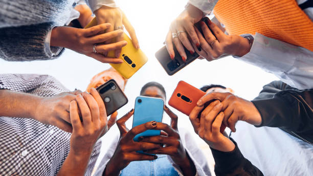 Teens in circle holding smart mobile phones - Multicultural young people using cellphones outside - Teenagers addicted to new technology concept stock photo