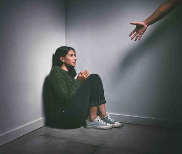어두운 방 구석에 앉아 있는 한 젊은 여성이 손을 내밀어 그녀를 돕기 위해 총을 쏘는 장면 - crisis 뉴스 사진 이미지