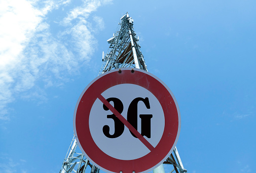 Illustration of the end of life for 3rd generation or 3G cell mobile networks. Road sign with 3G text against rural cellphone tower
