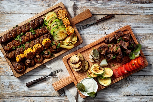 Assorted kebabs, grilled meat with vegetables and herbs. Appetizing fried meat, tomatoes, zucchini, potatoes and onions on cutting boards. Top view