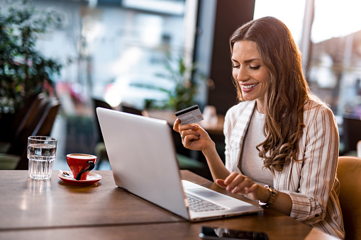 Beautiful young businesswoman using credit card to buy online on her laptop at cafe. Young woman using electronic banking.