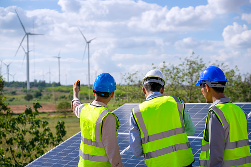 Blue collar workers at electricity site. Windmill field. They are working in the field during the day. Alternative energy.