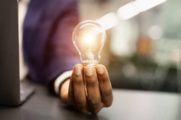 istock Black businessman holding illuminated light bulb, sitting in office, cropped 1371965959