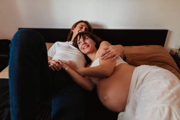 Happy couple expecting a baby cuddling in the bedroom on the bed Happy couple expecting a baby cuddling in the bedroom on the bed. Color editing and added grain. Real life situation. Part of a series. body positive couple stock pictures, royalty-free photos & images