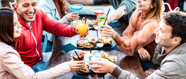 молодые люди держат разноцветные напитки - модные друзья моды веселятся вместе, поднимая тосты за коктейли в счастливый час - социальная вс� - party lifestyles social gathering family стоковые фото и изображения