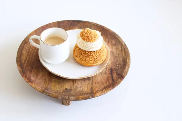 Tasty coffee and craquelin choux pastry cream-puff dessert filled with cream on a wooden plate. Food concept.