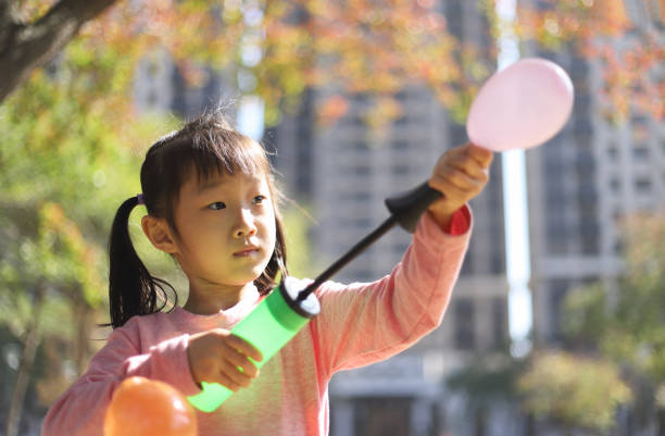 a Asian smiling girl playing balloon in a park.