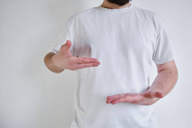 istock Man in a white T-shirt on a light background shows different hand gestures. Hand gestures and emotions. Studio photography. Place for text and advertising 1371975309