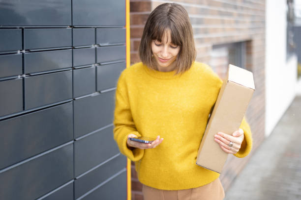 istock Happy woman with parcel and phone standing near automatic post terminal 1371975905