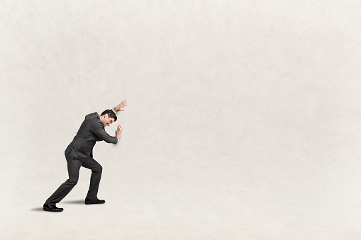 A man leans into and attempts to push against a wall that provides ample room for copy and text.